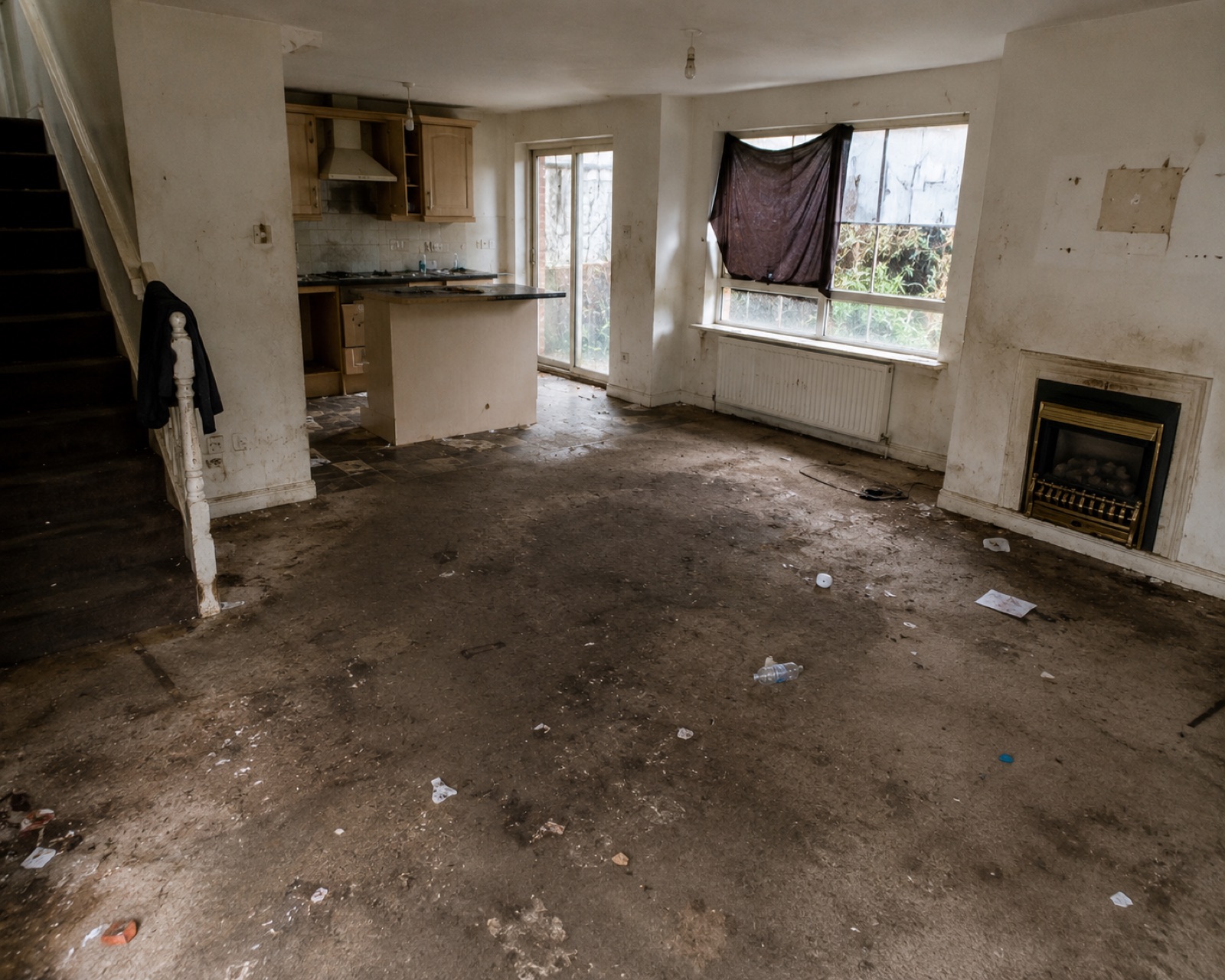 Empty through-lounge left filthy at the end of a tenancy, with a heavily soiled floor and debris throughout